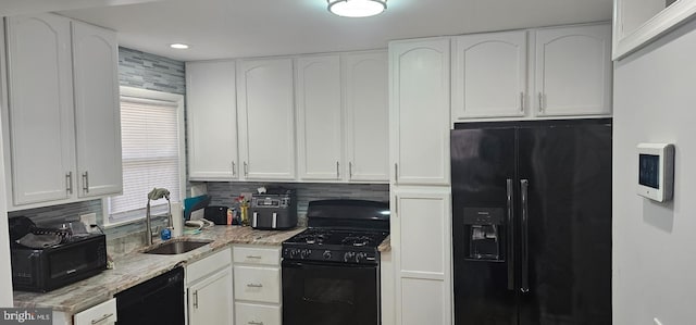 kitchen with a sink, light stone countertops, black appliances, and white cabinetry