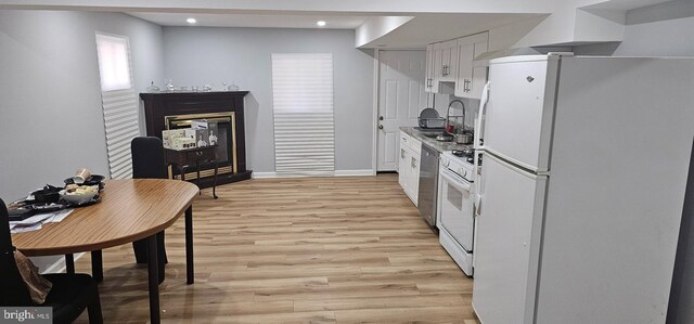 kitchen featuring light wood-type flooring, a glass covered fireplace, white appliances, white cabinetry, and a sink