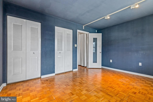 unfurnished bedroom featuring baseboards, two closets, and rail lighting