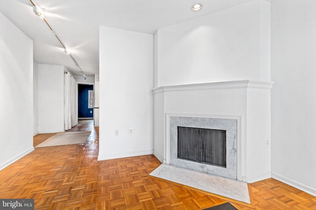 unfurnished living room featuring baseboards, a fireplace, and track lighting