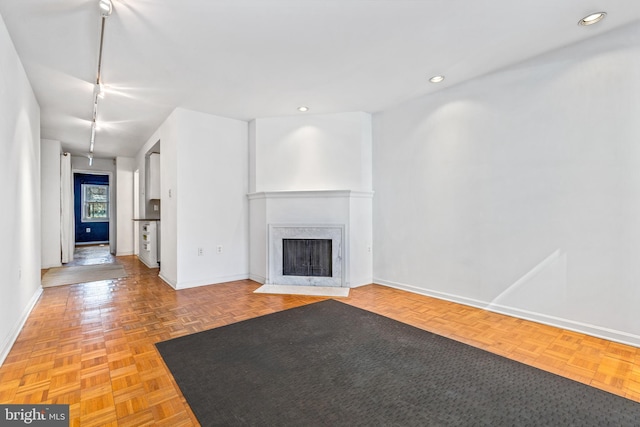 unfurnished living room featuring a fireplace with flush hearth, track lighting, and baseboards