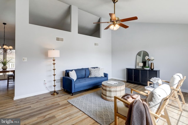 living room with baseboards, visible vents, light wood-style floors, high vaulted ceiling, and ceiling fan with notable chandelier