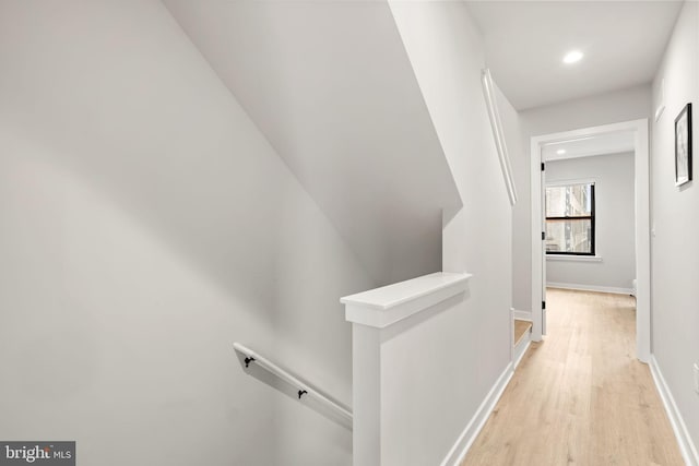 corridor with light wood-type flooring, baseboards, and an upstairs landing