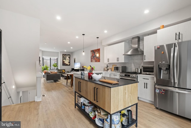 kitchen with a kitchen island, white cabinets, light wood-style floors, appliances with stainless steel finishes, and wall chimney range hood