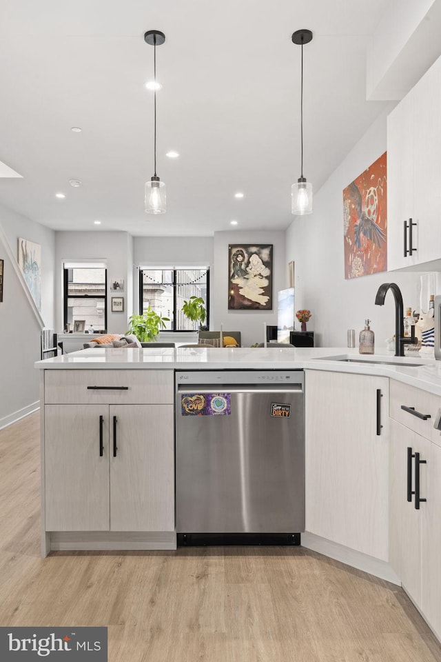 kitchen with light wood finished floors, a sink, stainless steel dishwasher, light countertops, and hanging light fixtures