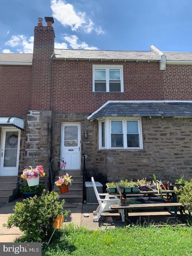 view of front facade featuring stone siding, brick siding, and a chimney