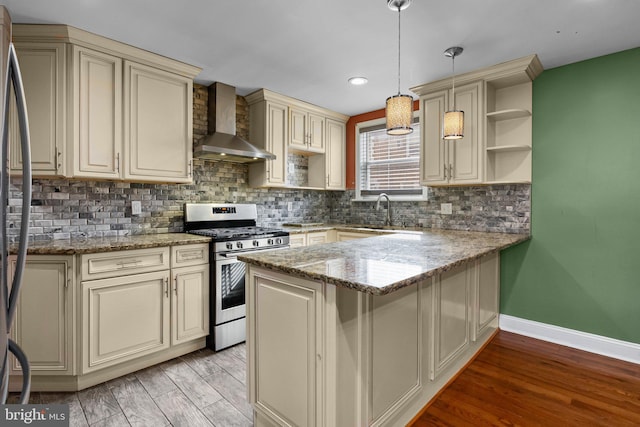 kitchen with stainless steel gas range, cream cabinetry, wall chimney exhaust hood, and open shelves