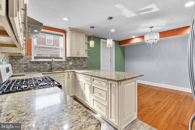 kitchen with cream cabinets, a sink, gas range, light wood-type flooring, and a peninsula