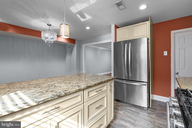 kitchen featuring visible vents, light stone counters, freestanding refrigerator, cream cabinetry, and gas stove