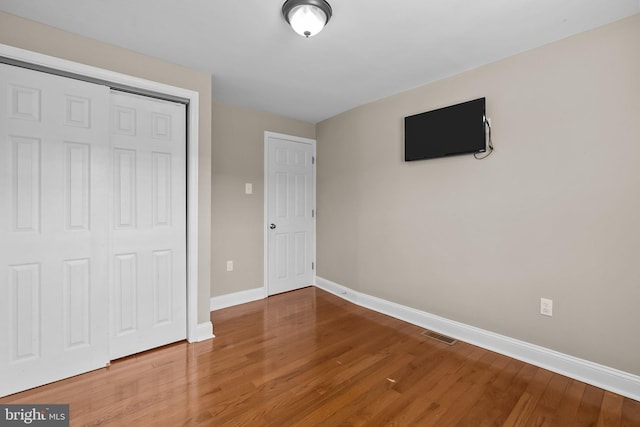 unfurnished bedroom with a closet, visible vents, baseboards, and wood finished floors