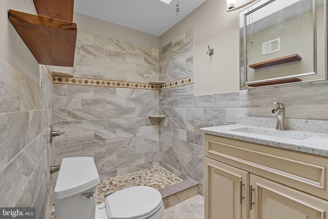 bathroom with toilet, visible vents, vanity, tile walls, and a tile shower