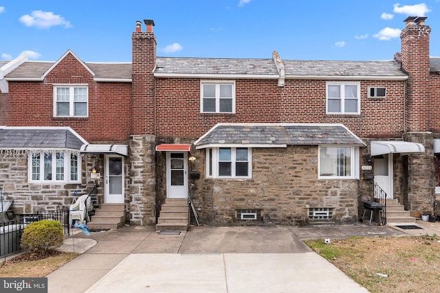 rear view of house with a high end roof, stone siding, a chimney, and entry steps