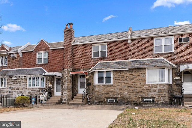 view of front of house with entry steps, stone siding, a chimney, and a high end roof