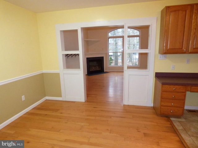 unfurnished dining area with light wood finished floors, a fireplace with flush hearth, built in shelves, and baseboards