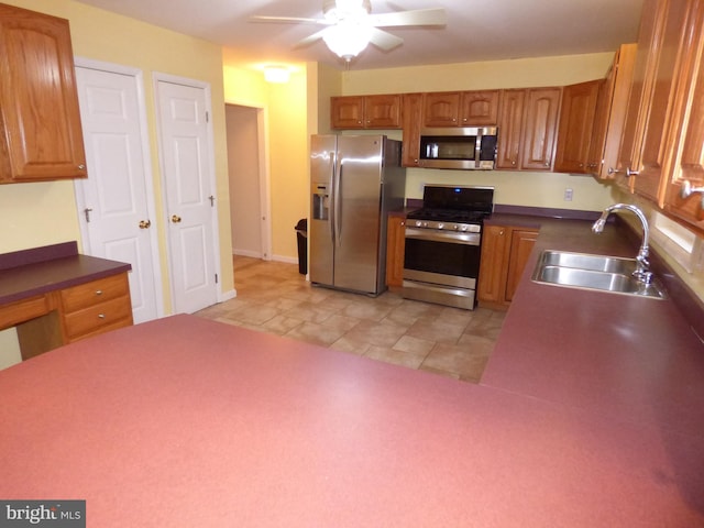 kitchen with a sink, a ceiling fan, appliances with stainless steel finishes, brown cabinets, and dark countertops