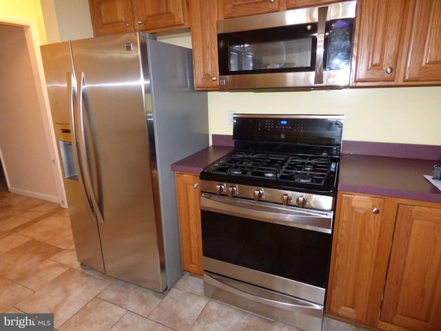 kitchen featuring dark countertops, light tile patterned floors, appliances with stainless steel finishes, and brown cabinetry