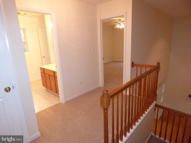 corridor with baseboards, light carpet, and an upstairs landing