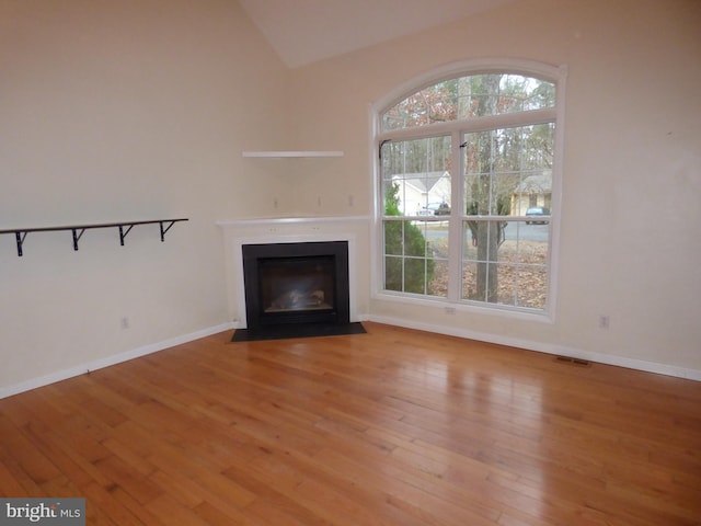 unfurnished living room with lofted ceiling, light wood-type flooring, a fireplace with flush hearth, and baseboards