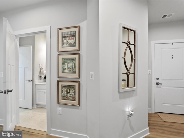 hall featuring light wood-style floors, baseboards, and visible vents