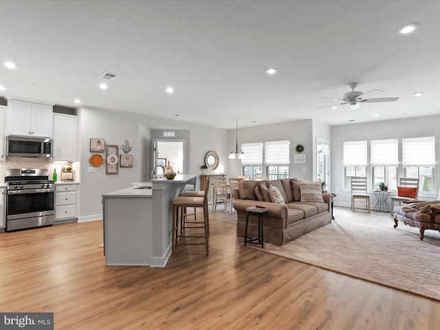 living room with recessed lighting, visible vents, light wood-style flooring, and baseboards