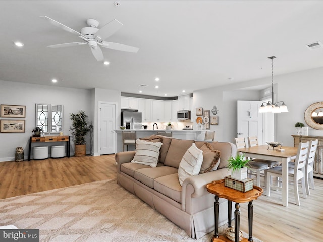 living area with recessed lighting, visible vents, baseboards, light wood-style floors, and ceiling fan with notable chandelier