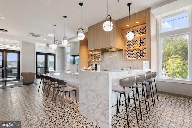 kitchen with a breakfast bar area, french doors, light stone countertops, tasteful backsplash, and modern cabinets