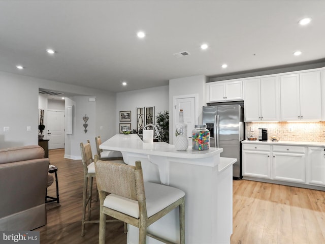 kitchen featuring light wood-style flooring, white cabinetry, visible vents, stainless steel refrigerator with ice dispenser, and decorative backsplash