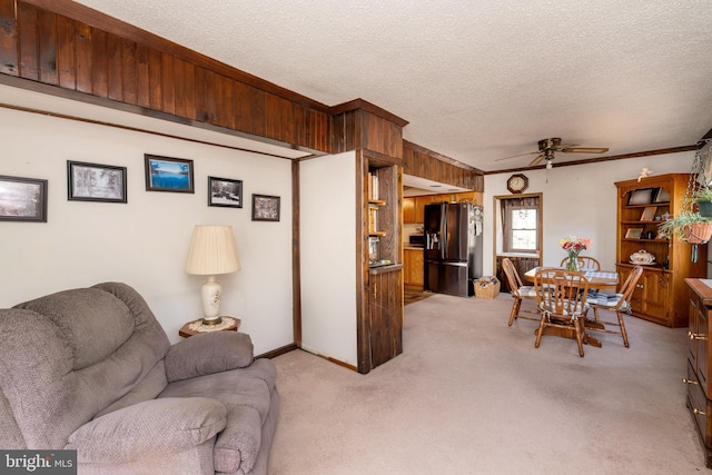 living room with a textured ceiling, light carpet, a ceiling fan, baseboards, and crown molding