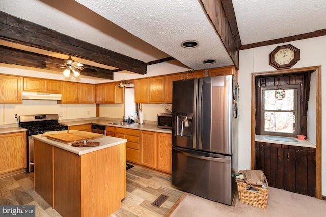 kitchen with a textured ceiling, under cabinet range hood, light countertops, appliances with stainless steel finishes, and beamed ceiling