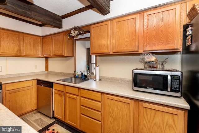 kitchen with a sink, stainless steel appliances, light countertops, light wood-style floors, and beam ceiling