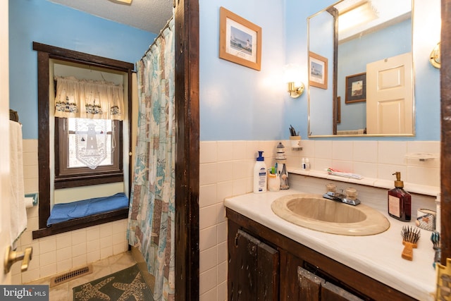 bathroom with visible vents, a wainscoted wall, a textured ceiling, vanity, and tile walls