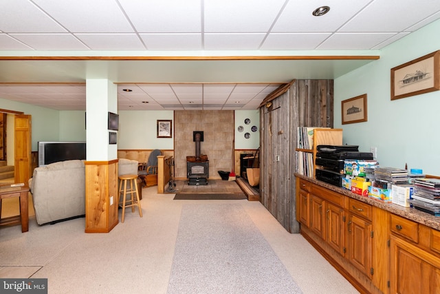 interior space with a wainscoted wall, a drop ceiling, and a wood stove