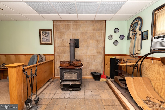 living area with a wainscoted wall, a drop ceiling, a wood stove, and wooden walls