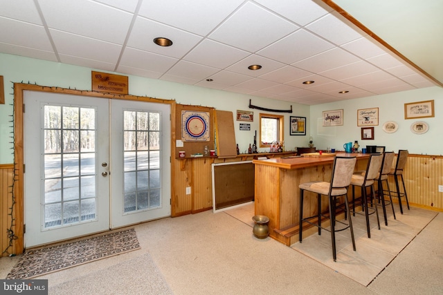 bar with wainscoting, a drop ceiling, wooden walls, and a bar