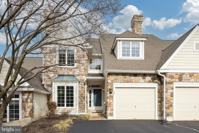 view of front of property featuring a garage, aphalt driveway, roof with shingles, and a chimney