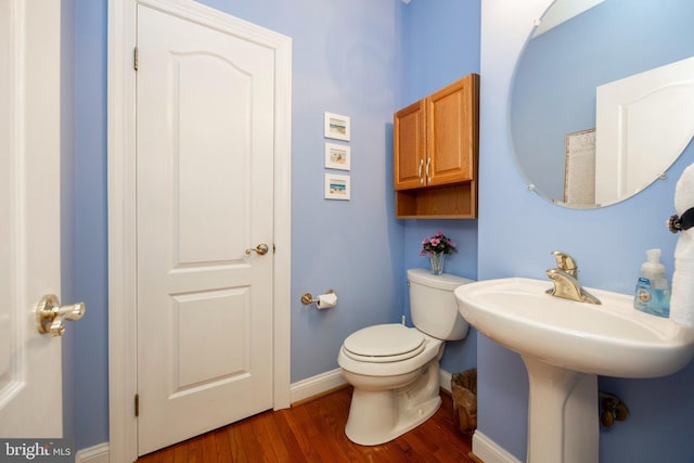 half bath with toilet, baseboards, and wood finished floors