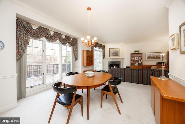 dining area featuring a chandelier, ornamental molding, a fireplace, and light colored carpet