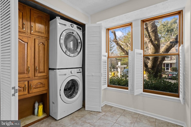 washroom with stacked washer / drying machine, a healthy amount of sunlight, baseboards, and light tile patterned floors