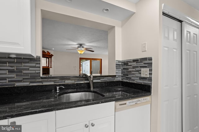 kitchen featuring decorative backsplash, white cabinets, a sink, dark stone counters, and dishwasher