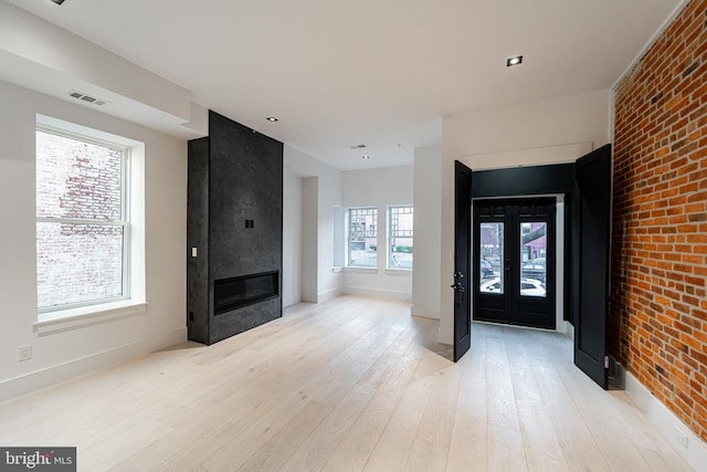 foyer entrance with light wood-style flooring, a large fireplace, brick wall, visible vents, and french doors