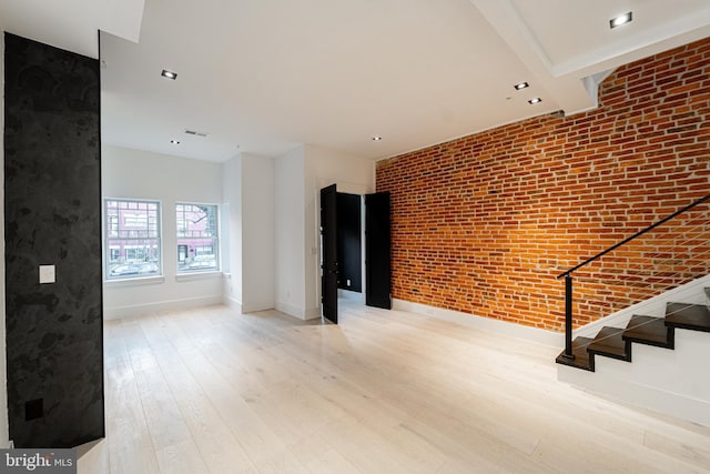 interior space featuring visible vents, light wood-style flooring, brick wall, baseboards, and stairs