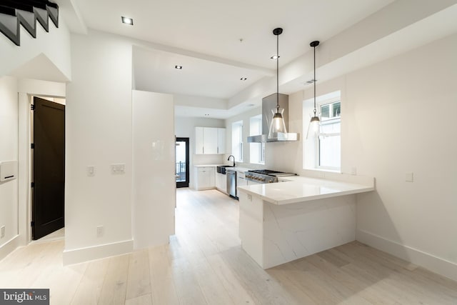 kitchen with dishwasher, a peninsula, light countertops, light wood-type flooring, and wall chimney range hood