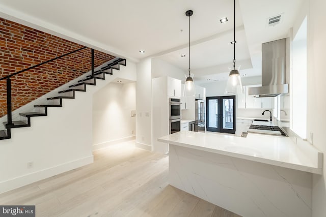 kitchen with island range hood, light wood-style flooring, stainless steel double oven, gas stovetop, and white cabinetry