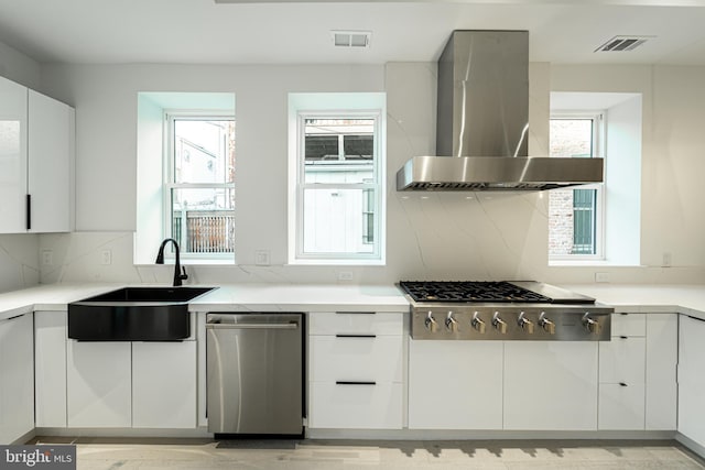 kitchen featuring stainless steel appliances, visible vents, white cabinets, a sink, and wall chimney exhaust hood