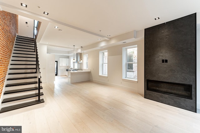 unfurnished living room with a fireplace, a sink, light wood-type flooring, baseboards, and stairs