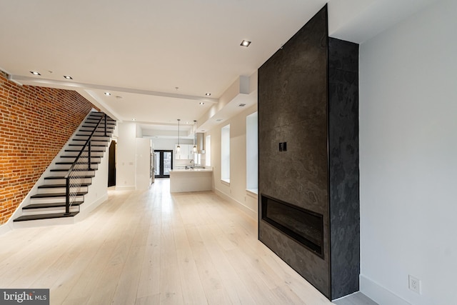 entrance foyer with a large fireplace, baseboards, brick wall, stairway, and light wood-type flooring