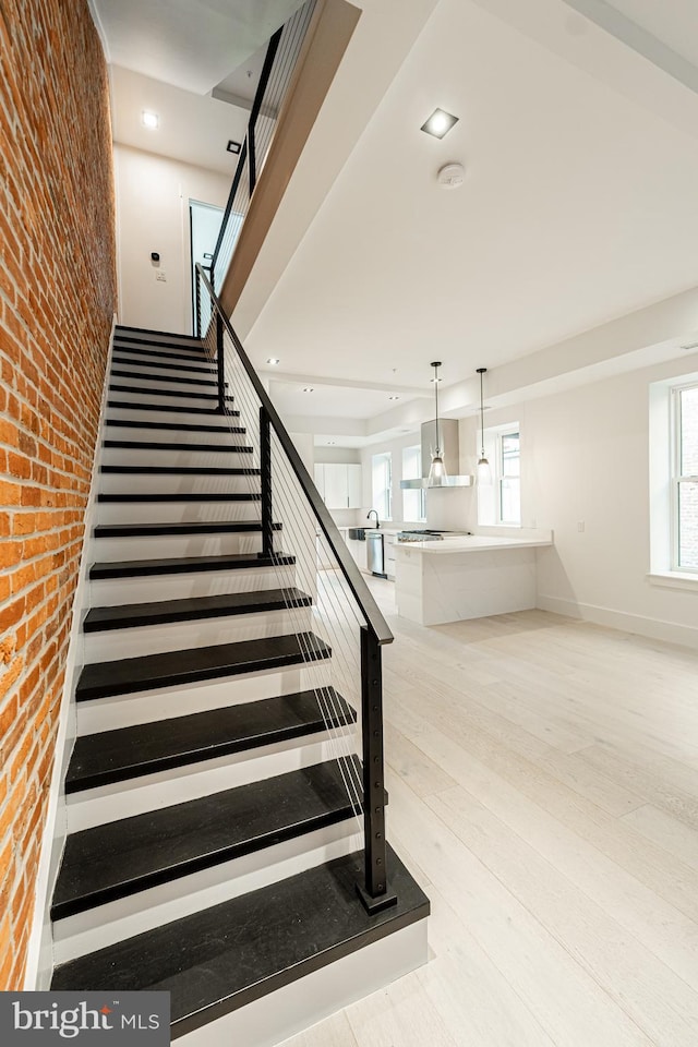 stairs with baseboards, brick wall, wood finished floors, and a healthy amount of sunlight