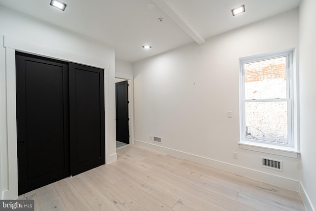 unfurnished bedroom featuring light wood-style floors, baseboards, visible vents, and beamed ceiling