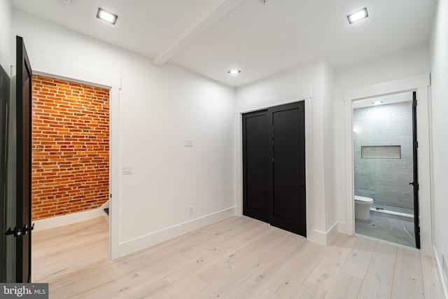 interior space featuring light wood finished floors, connected bathroom, beam ceiling, and baseboards