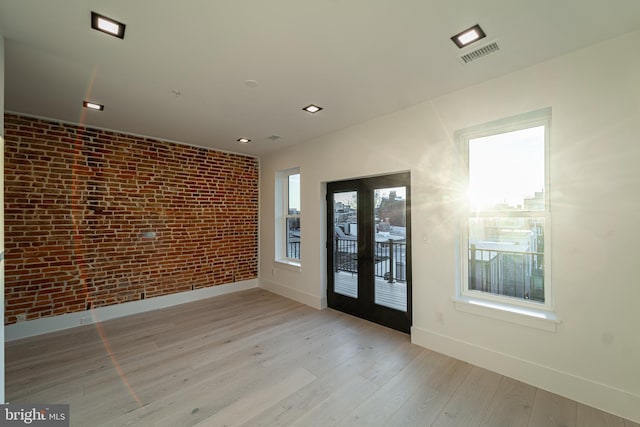 unfurnished room with brick wall, wood finished floors, visible vents, baseboards, and french doors